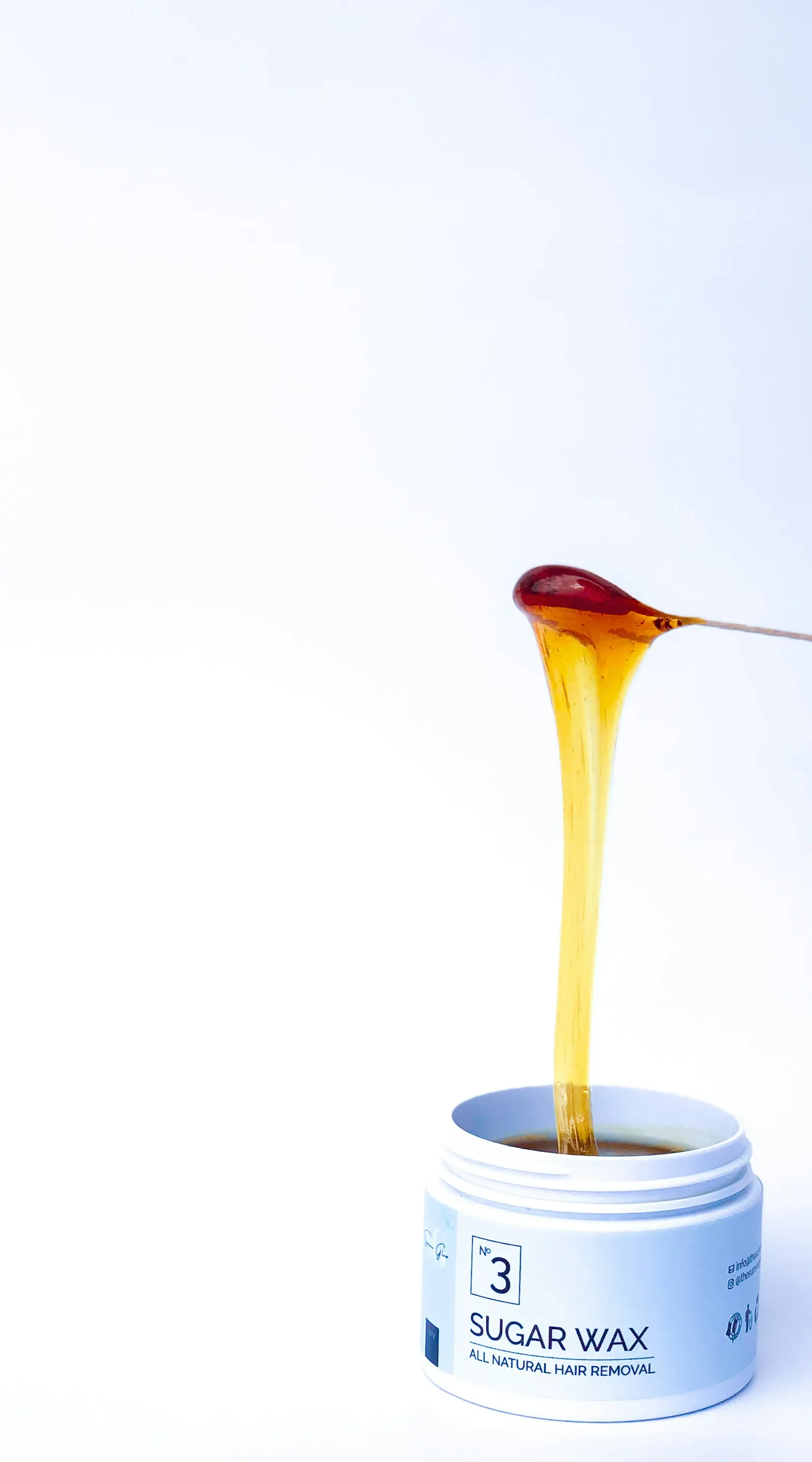Honey-colored sugar wax dripping into a jar